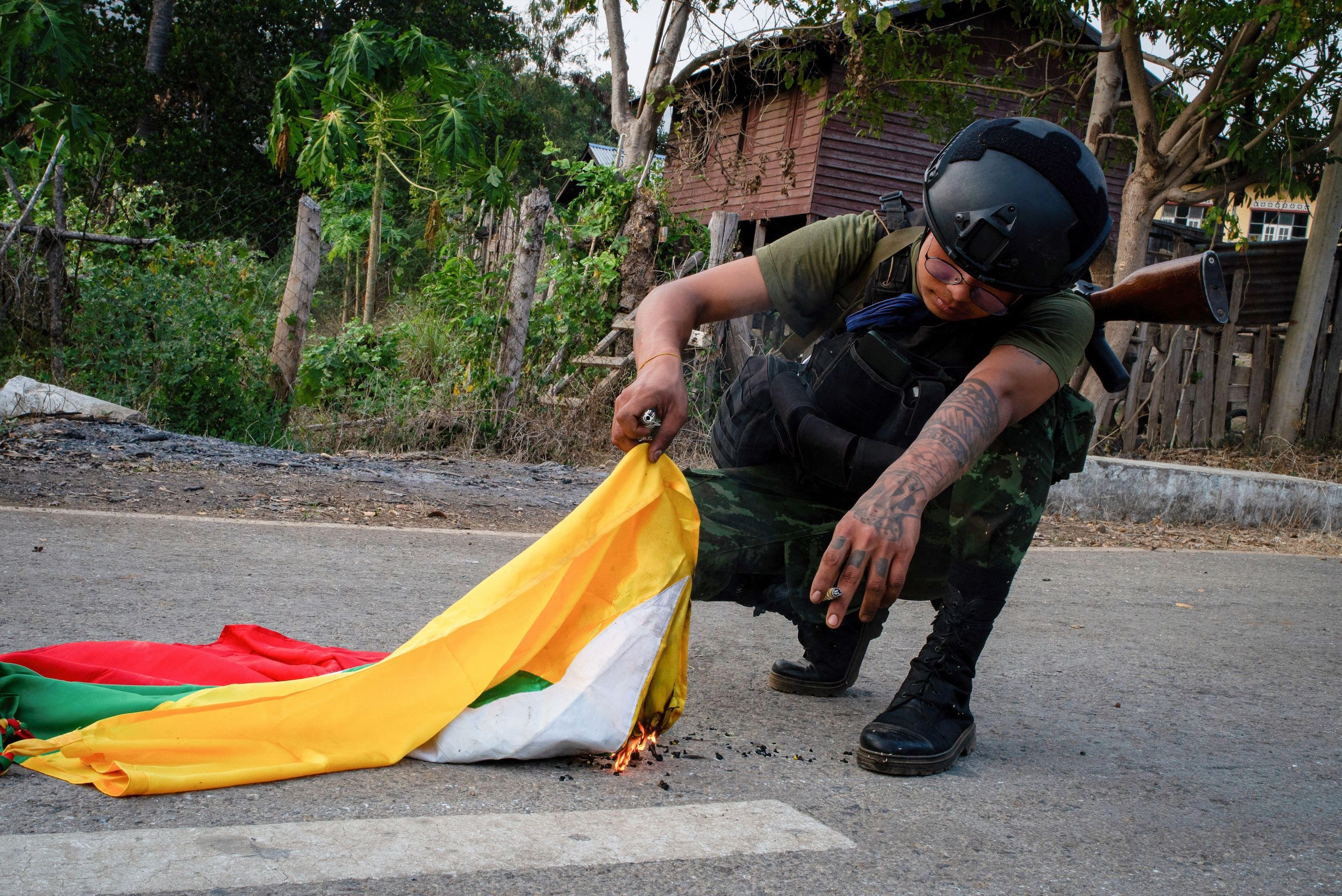 A soldier kneels on the ground burning a flag